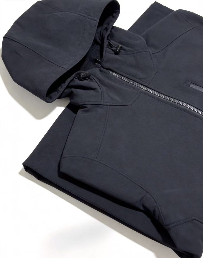 Black hooded work jacket close-up showing the hood, zipper and pocket details.